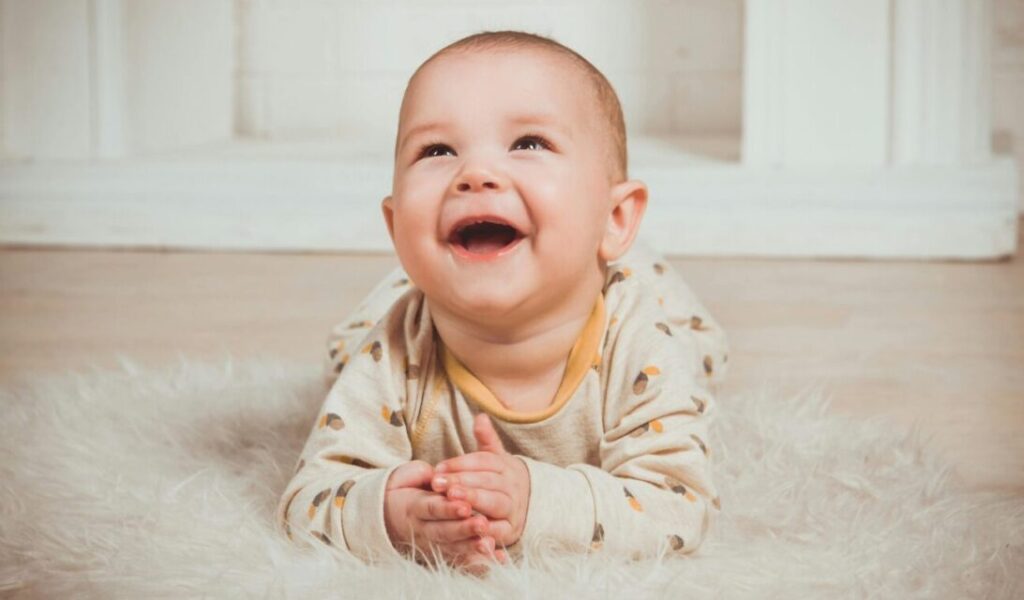 Joyful baby lying on a fluffy rug, smiling and looking upwards indoors.